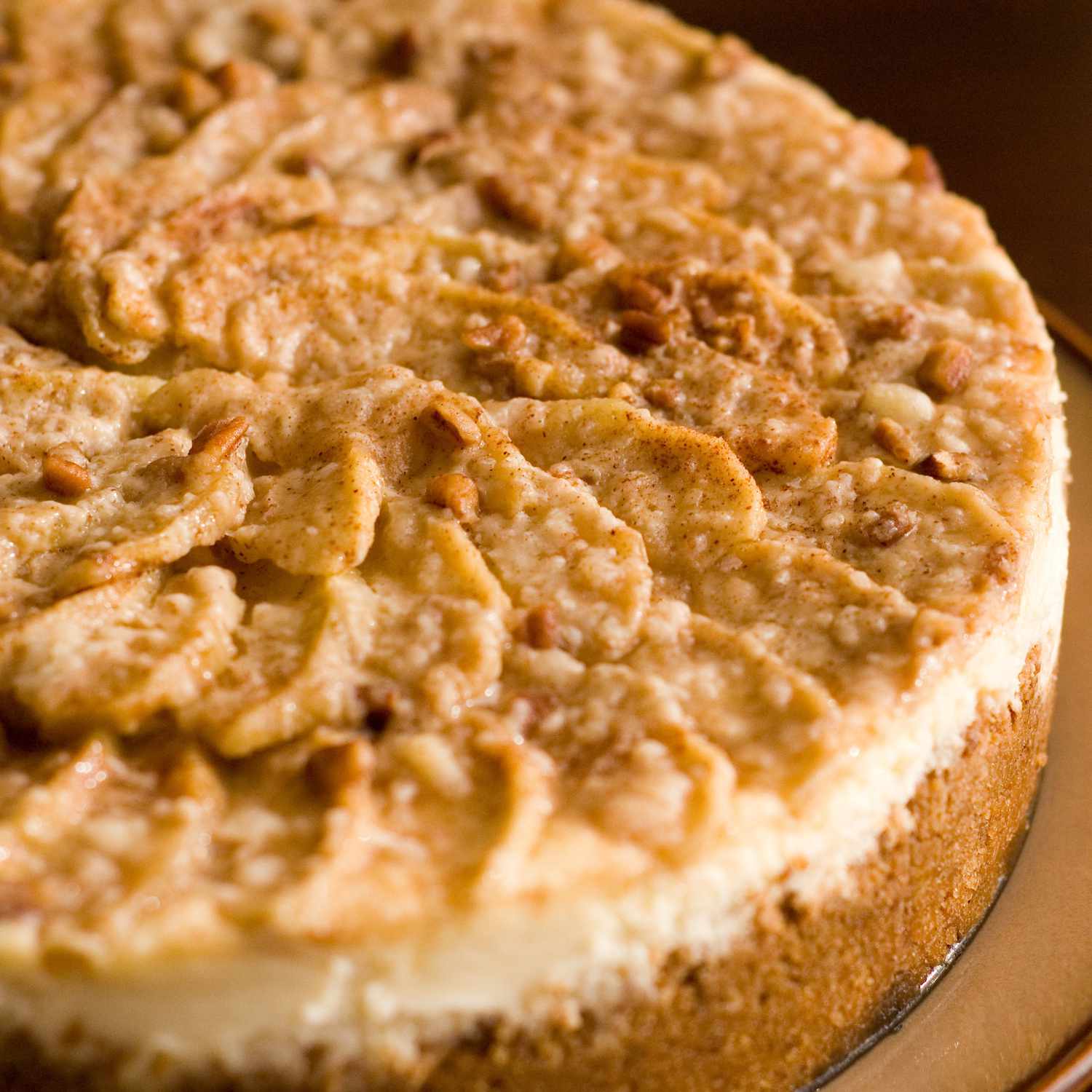 closeup of a beautiful-looking apple cheesecake with apple slices arranged in circles, topped with cinnamon sugar and chopped pecans