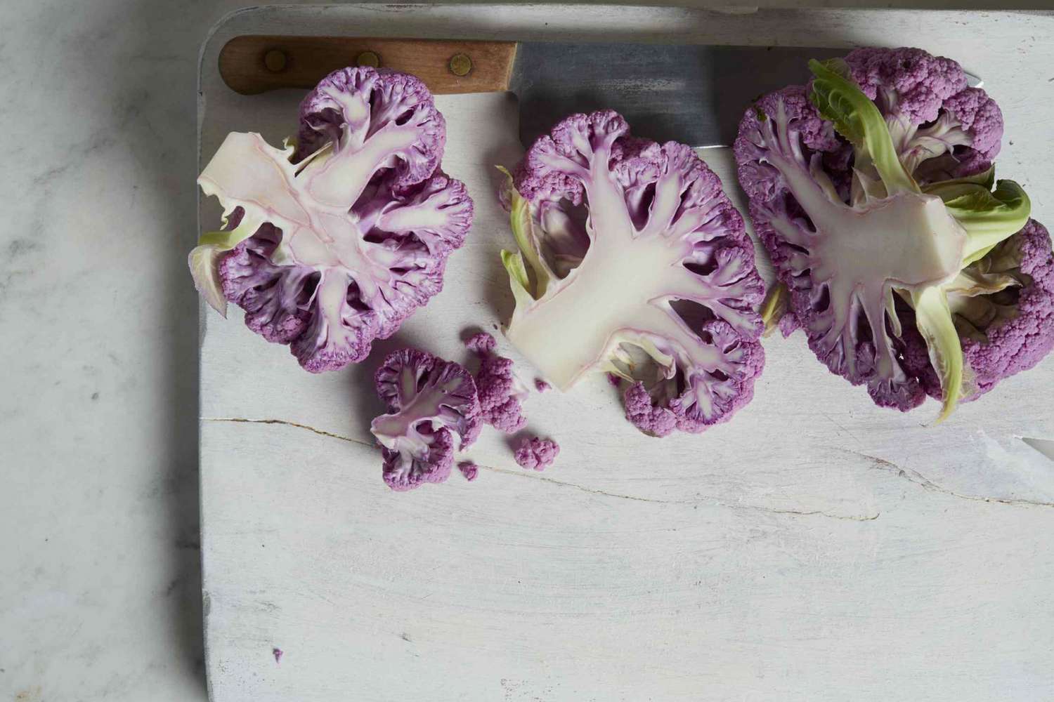 Chunks of purple cauliflower on white cutting board with knife