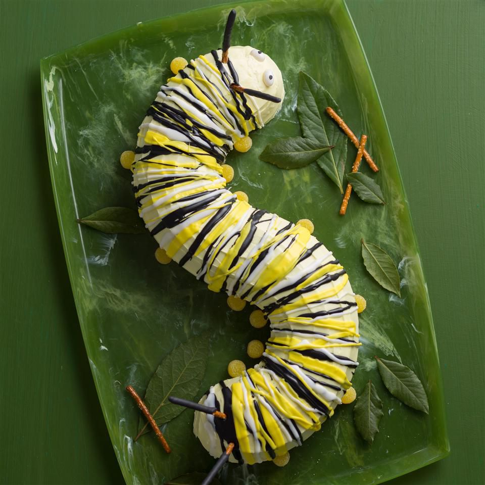 a twisting Caterpillar Cake with yellow, white, and black stripes sits on a green platter that's been painted to look like a leaf