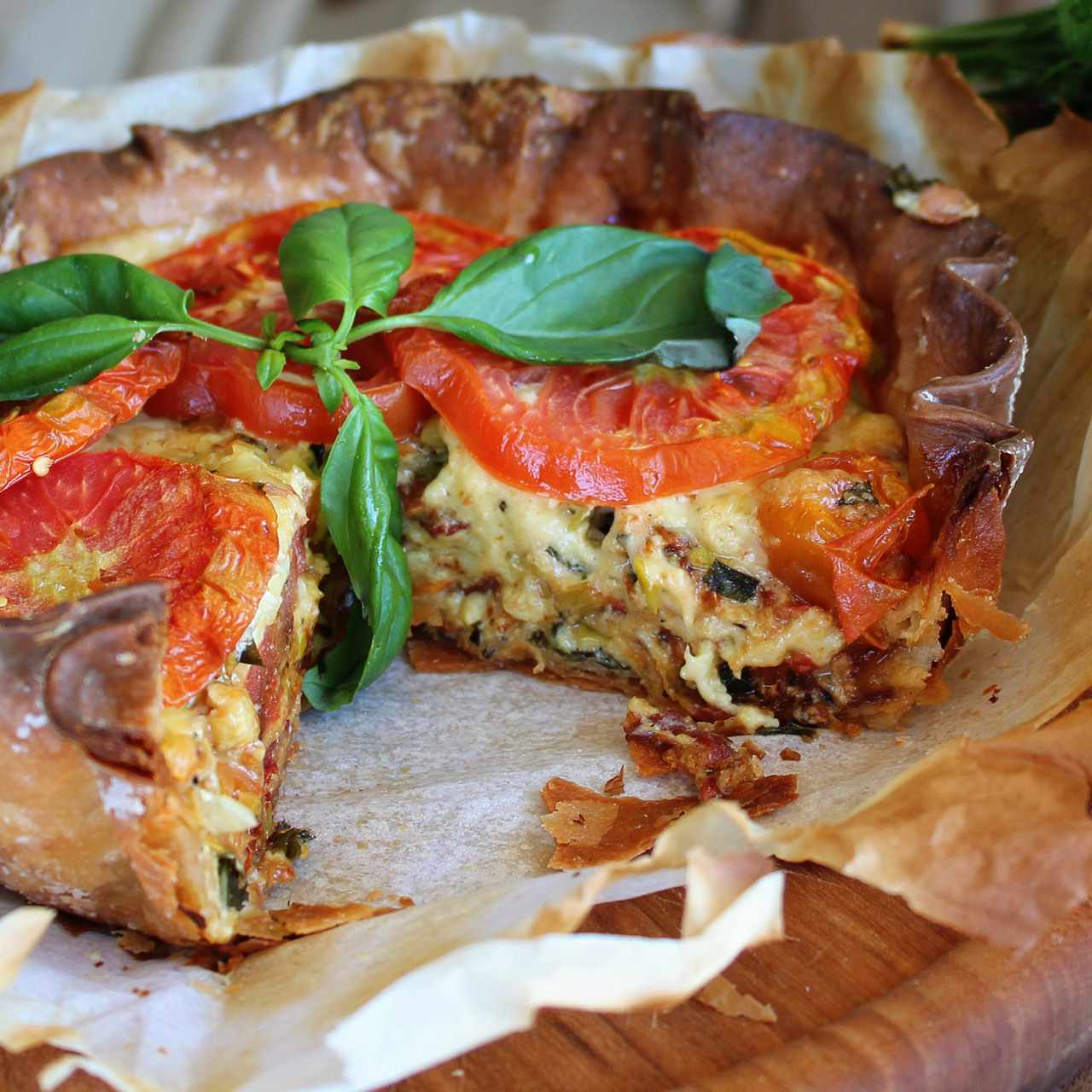 Side view of a deep dish savory pie garnished with sliced tomatoes and fresh basil with a large slice cut out of it
