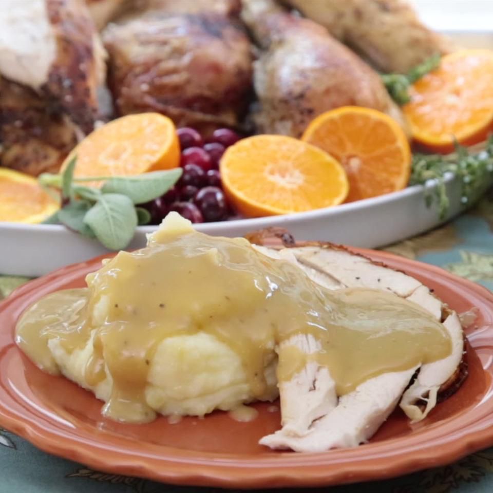 Turkey pieces with gravy on orange plate, whole Turkey platter in background