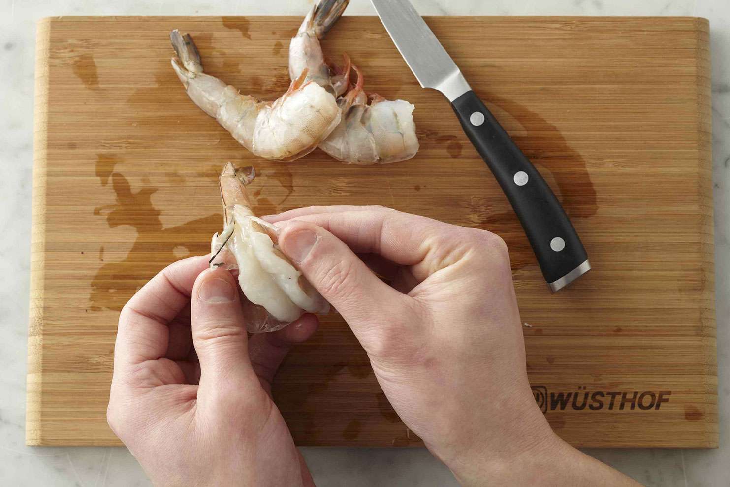 Person's hands peeling and deveing shrimp over cutting board