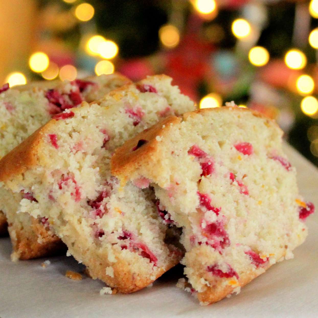 Closeup of slices of cranberry orange bread with white Christmas tree lights in the background