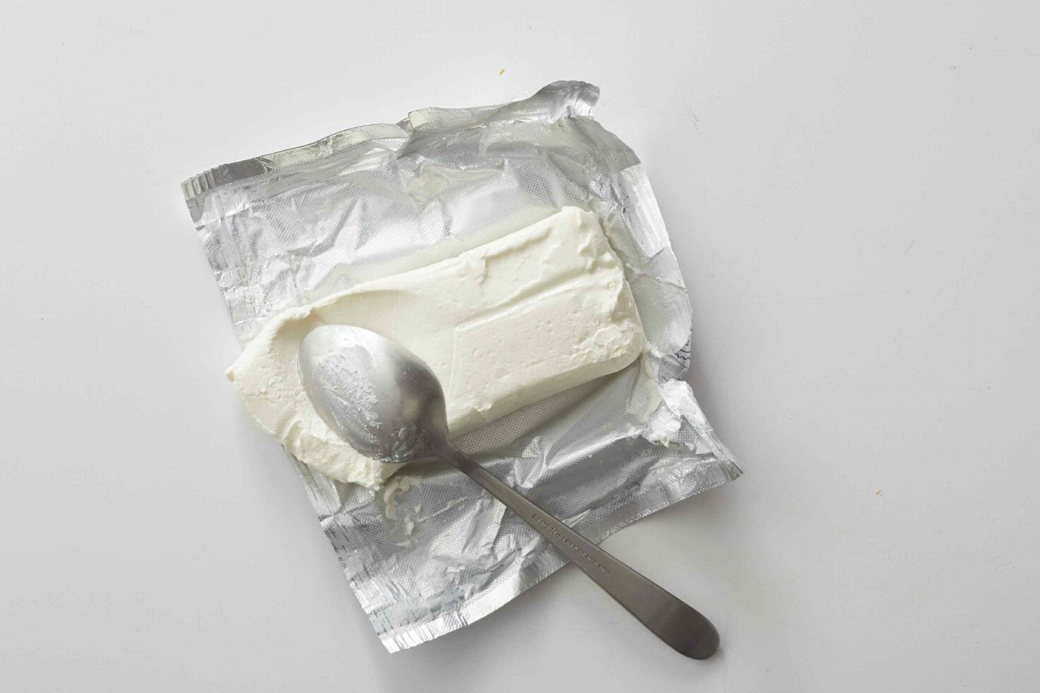 Block of cream cheese on aluminum wrapper with spoon