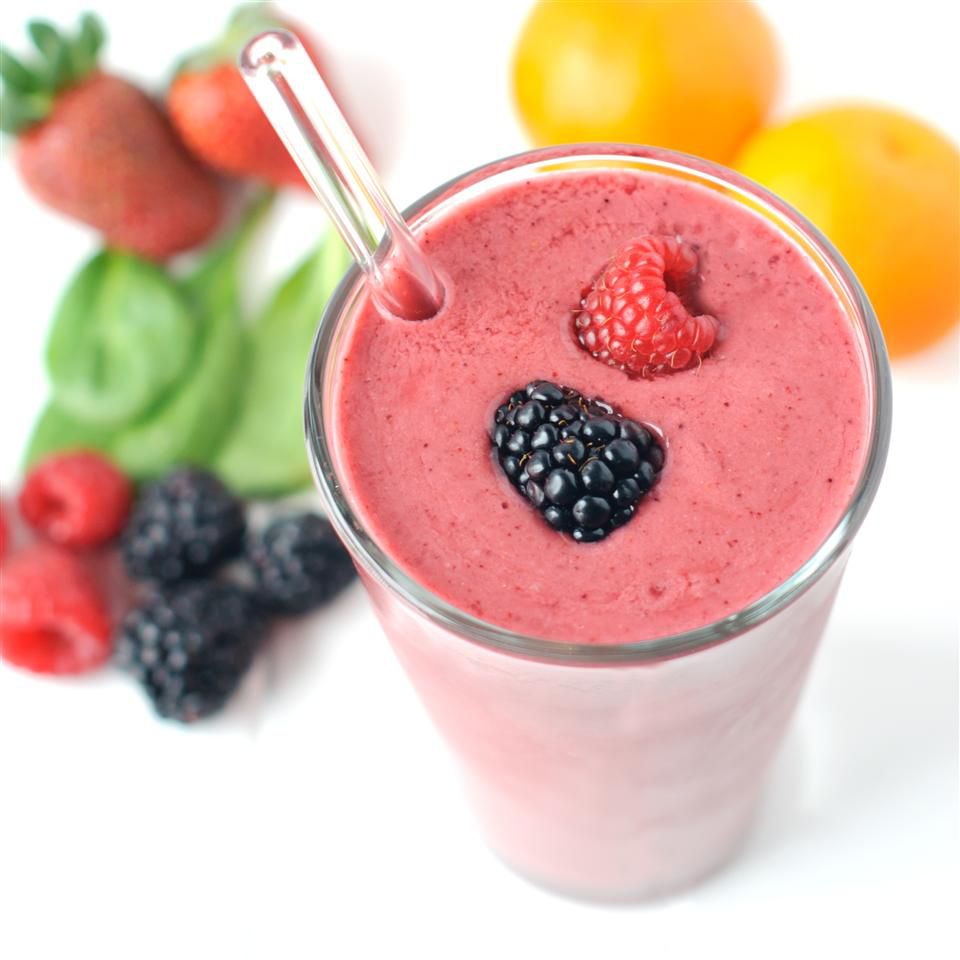 a glass of ealthy Berry and Spinach Smoothie with berries on top and other fruits sprinkled around it