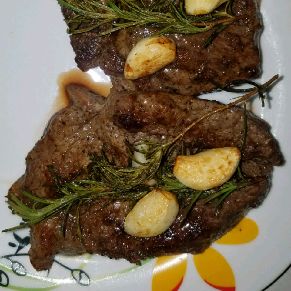 two Juicy Steaks on a white plate with rosemary sprigs and garlic cloves