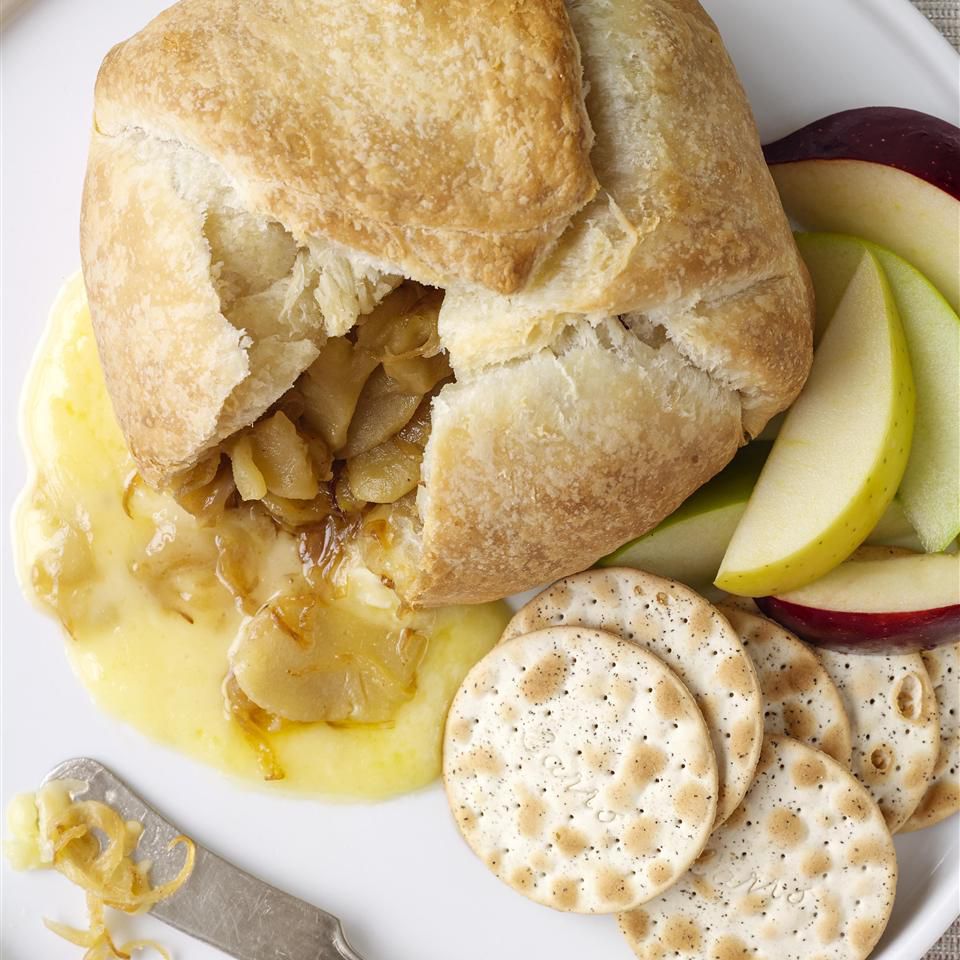 Baked Brie with Caramelized Onions on a white plate with water crackers and apple slices