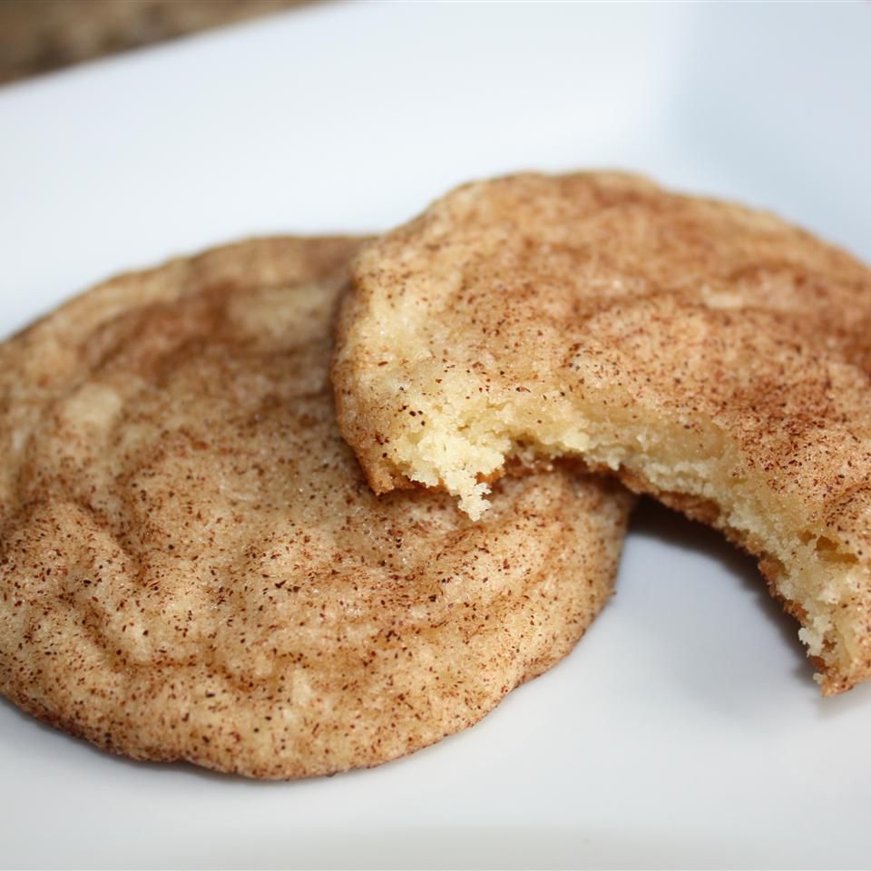 Two cinnamon-dusted sugar cookies on a white plate, one with a bite taken out of it