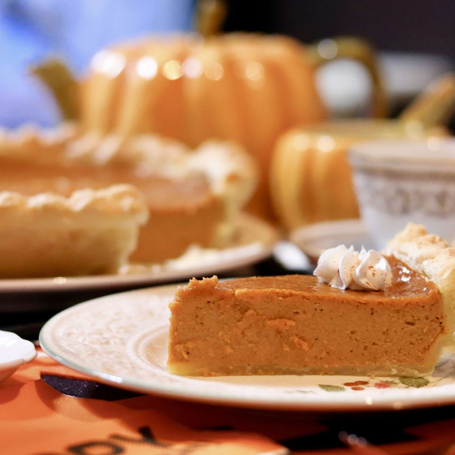 A slice of pumpkin pie on a plate in the foreground, with a whole pie behind it