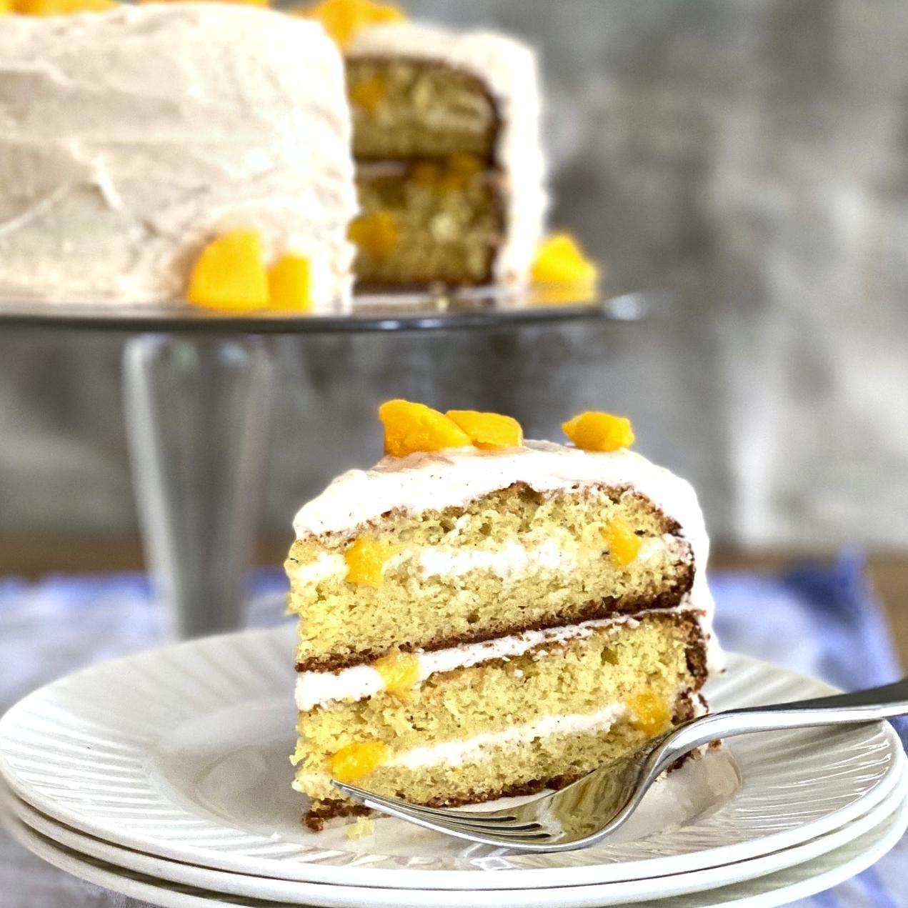 Slice of peach layer cake with the rest of the cake in the background