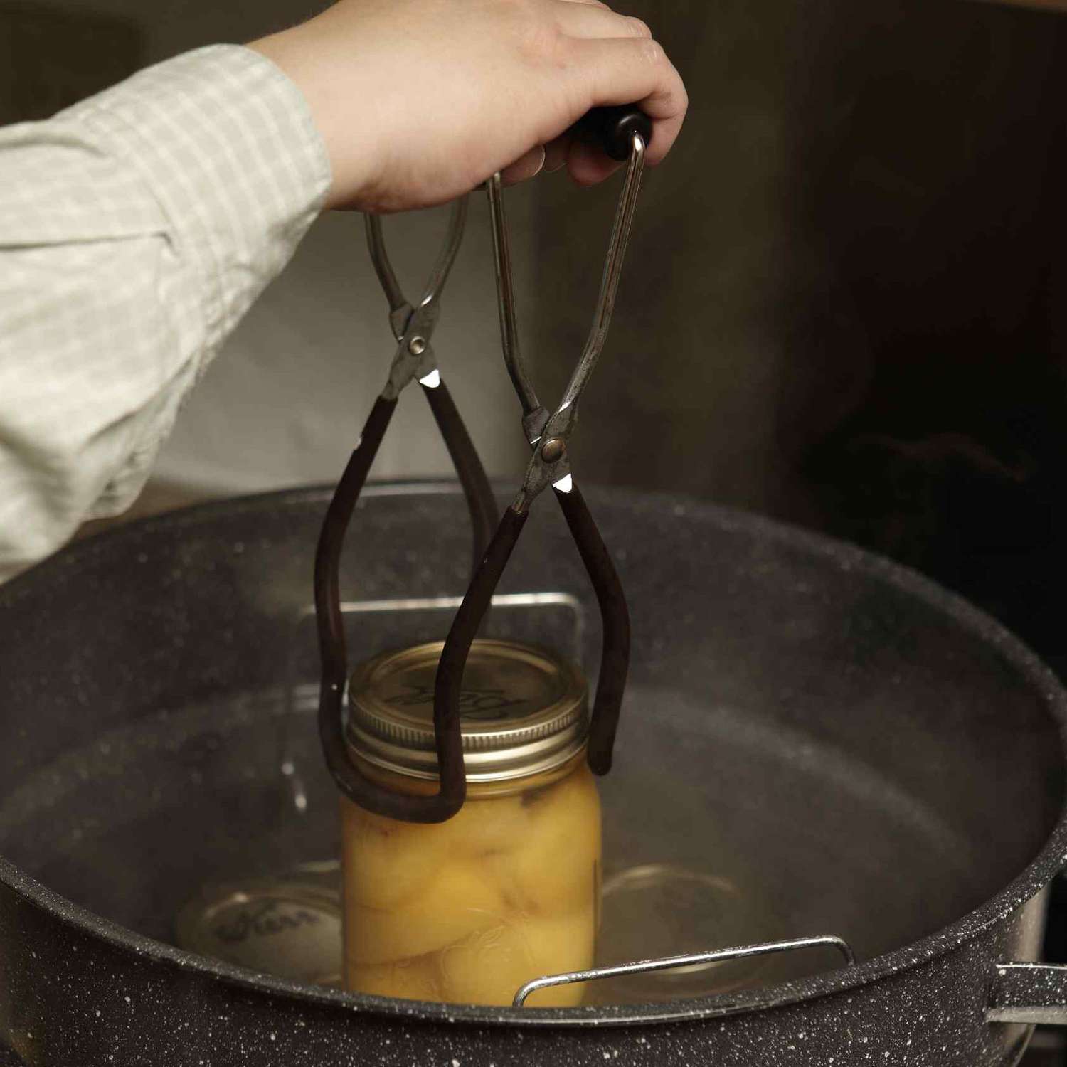Person placing can of peaches into water bath canner using tongs