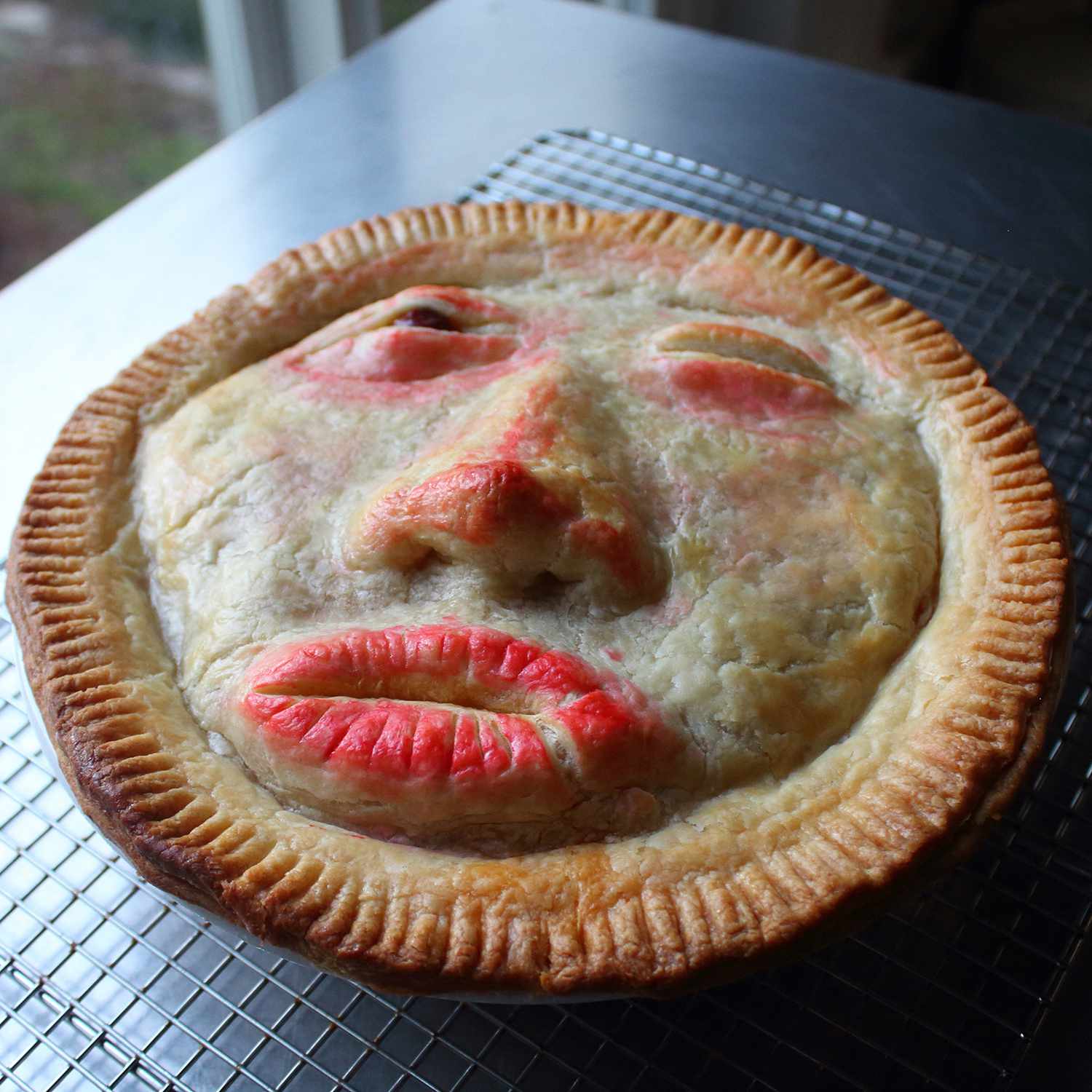 A meat pie for Halloween with a face shaped out of pie crust on a dark background