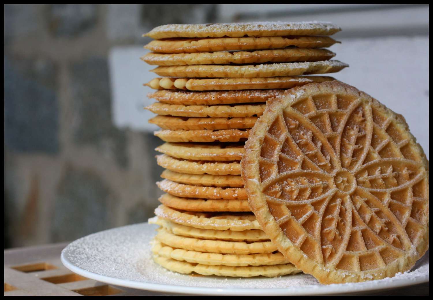 A tall stack of wafer cookies on a white plate, with one turned sideways to show off the flower design