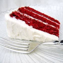 A slice of three-layer cake on a white china plate with a fork in the foreground