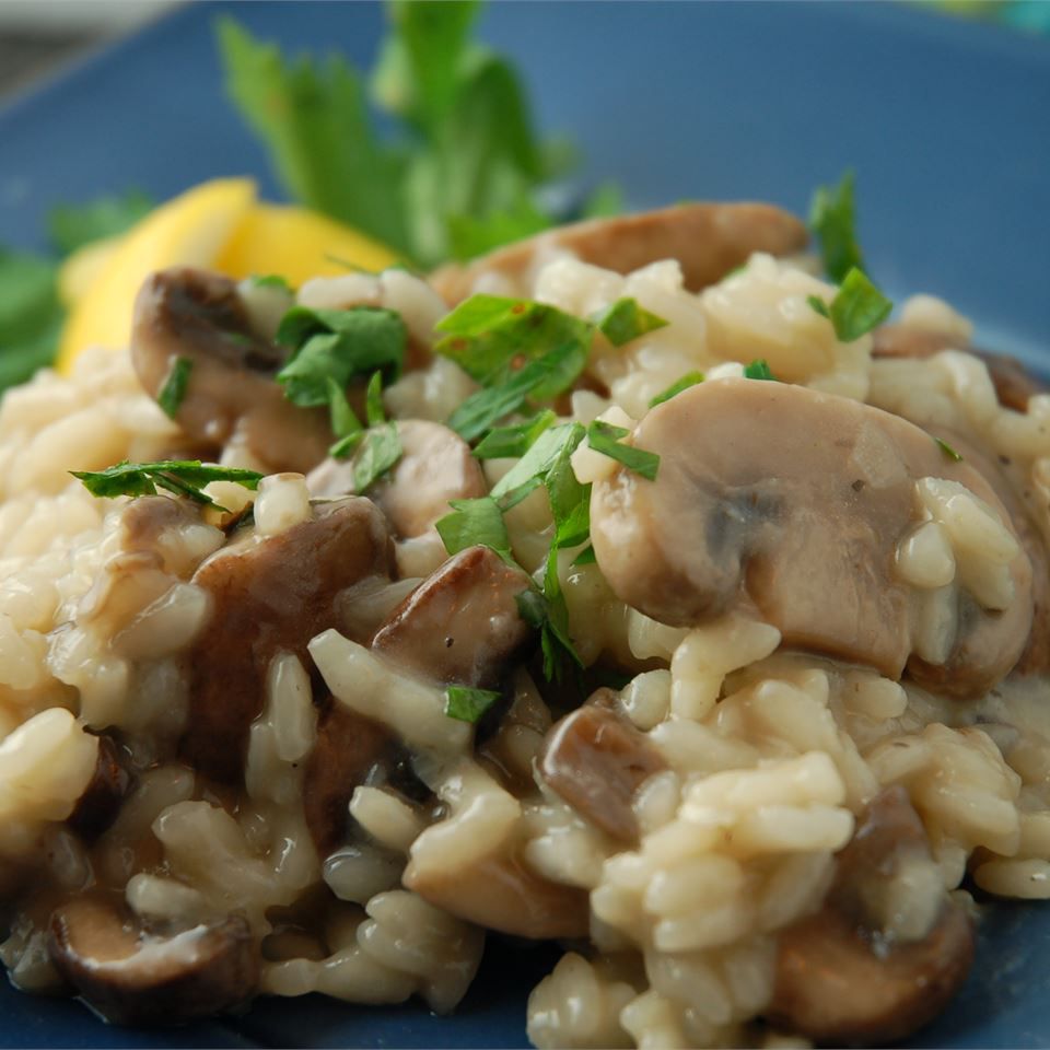 closeup of mushroom risotto garnished with parsley and a lemon wedge