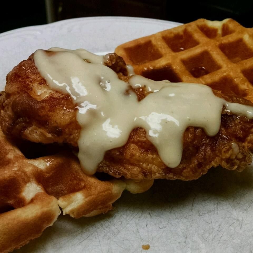 A piece of breaded chicken with creamy gravy served over two square waffles on a white plate