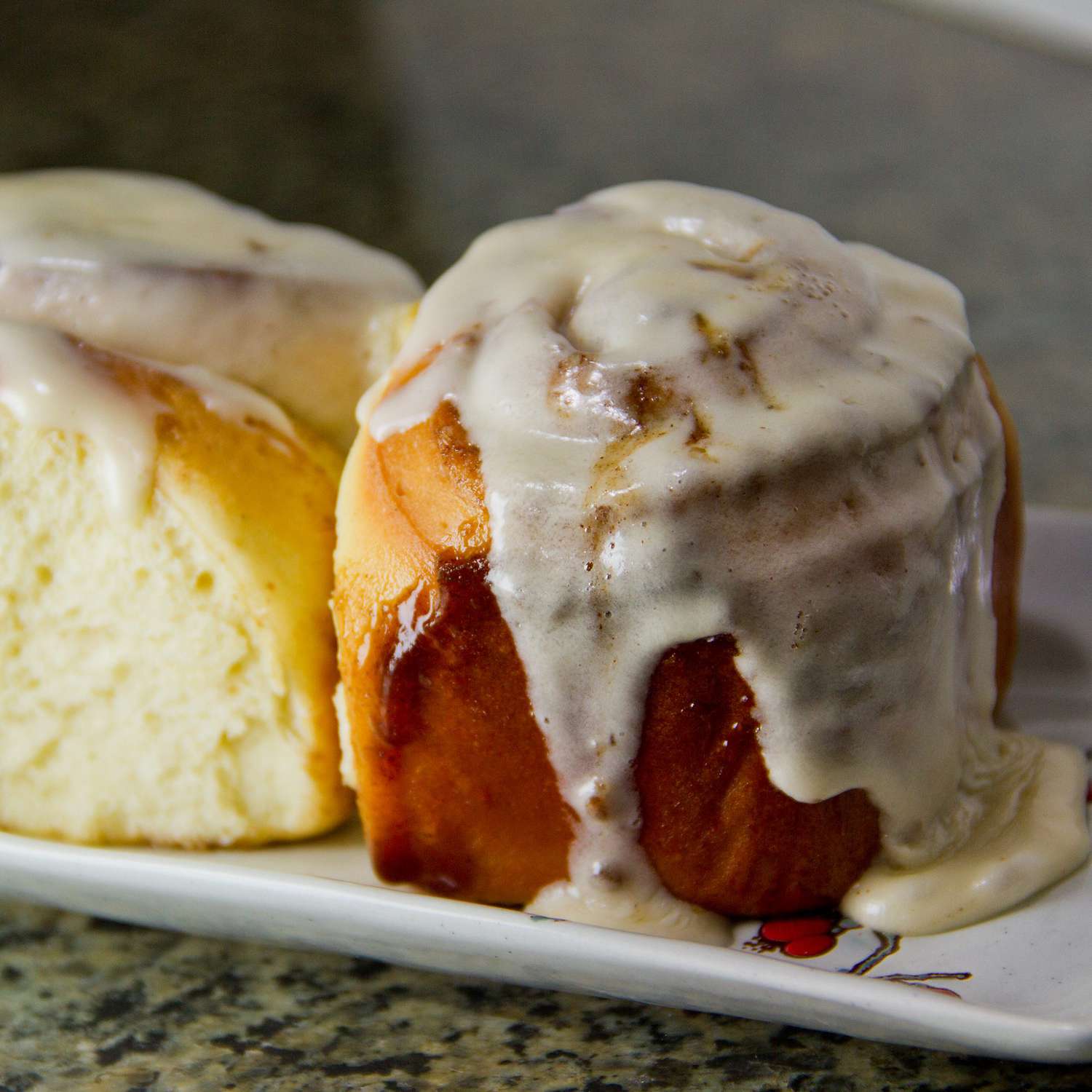 a closeup of two cinnamon rolls with icing dripping down the sides, on a rectangular white plate