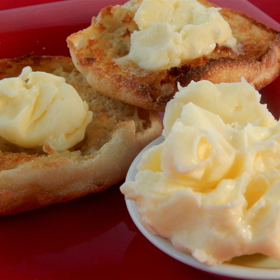 a dish of butter in the foreground, with toasted English muffins topped with butter in the background