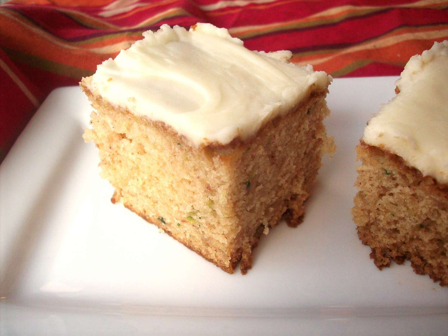 square slices of zucchini cake with cream cheese frosting on a rectangular white platter