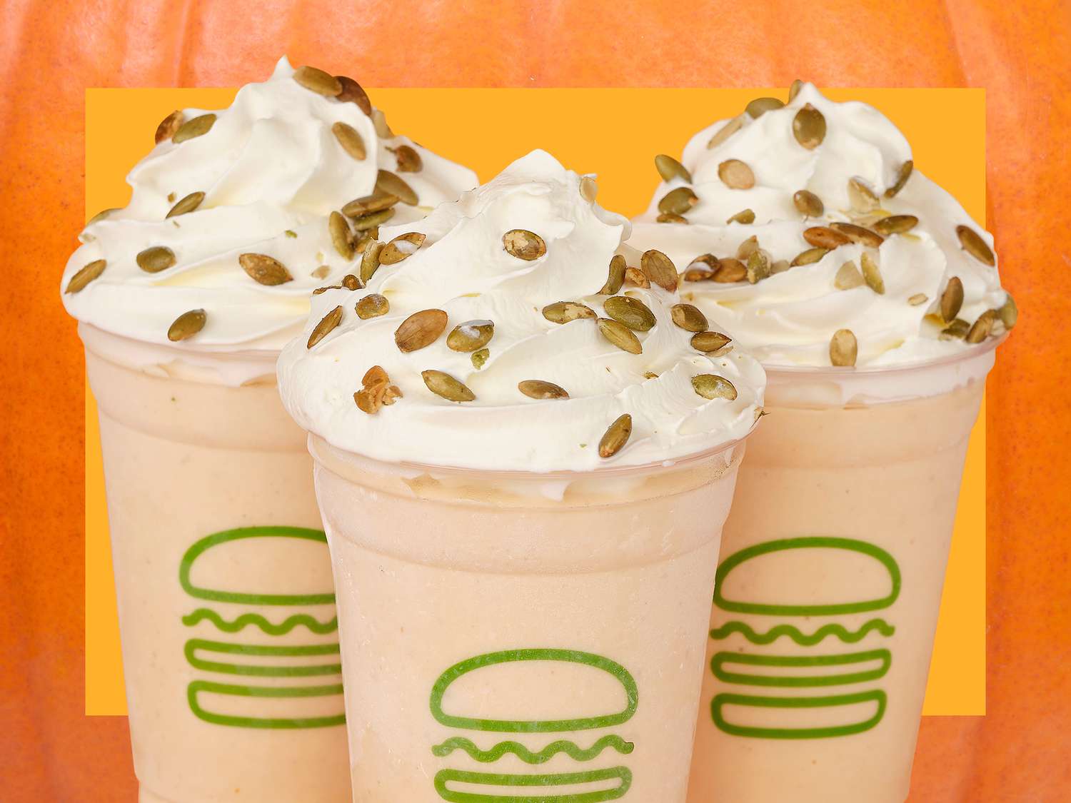 three whipped cream-topped pumpkin milkshakes with shake shack logo on the cup on an orange background