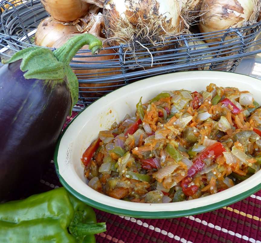 an oval white dish of a caponata-like eggplant appetizer, with onions and an eggplant in the background