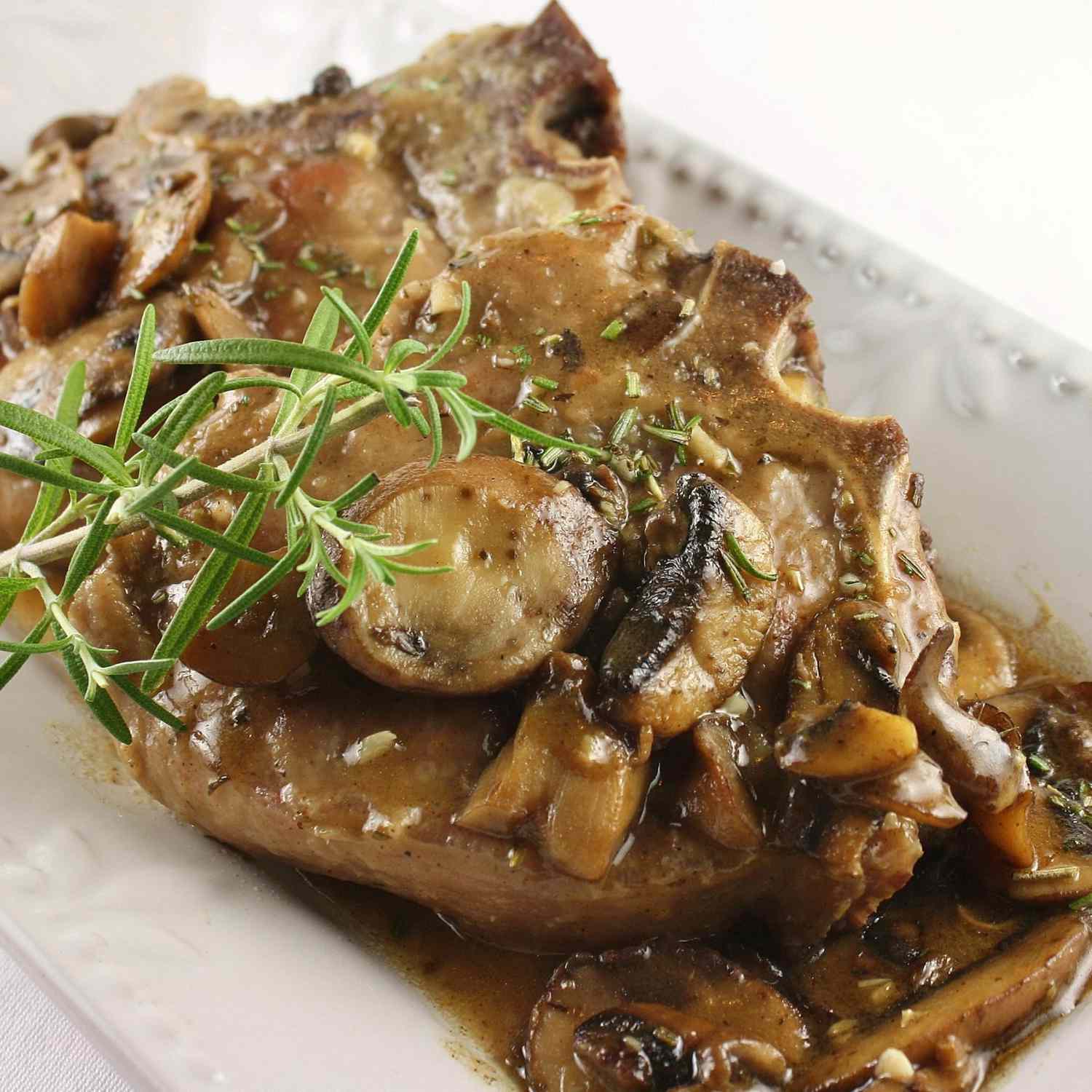 a veal chop on a rectangular white tray with mushroom gravy and a rosemary sprig