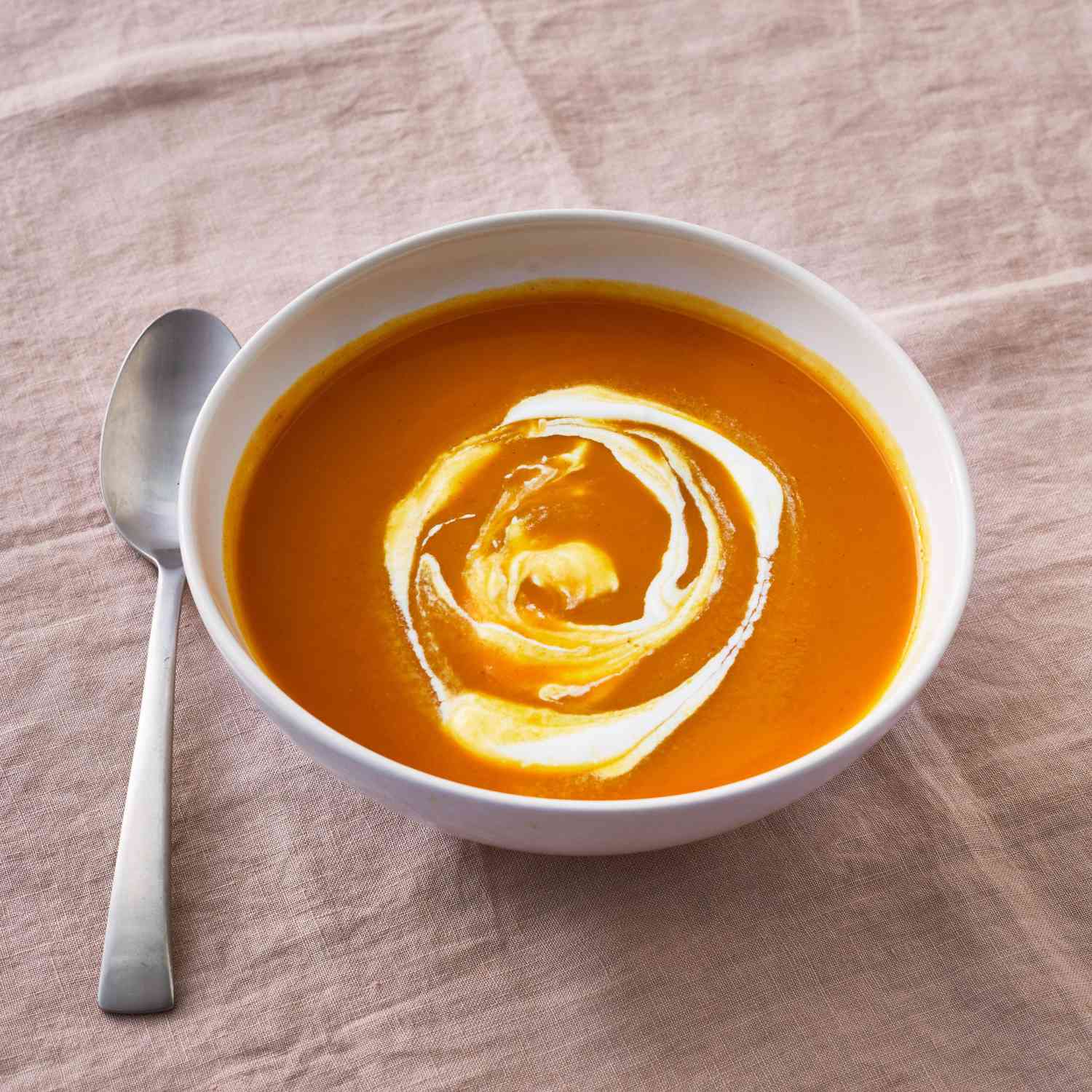 pumpkin soup in a white bowl on a mauve tablecloth