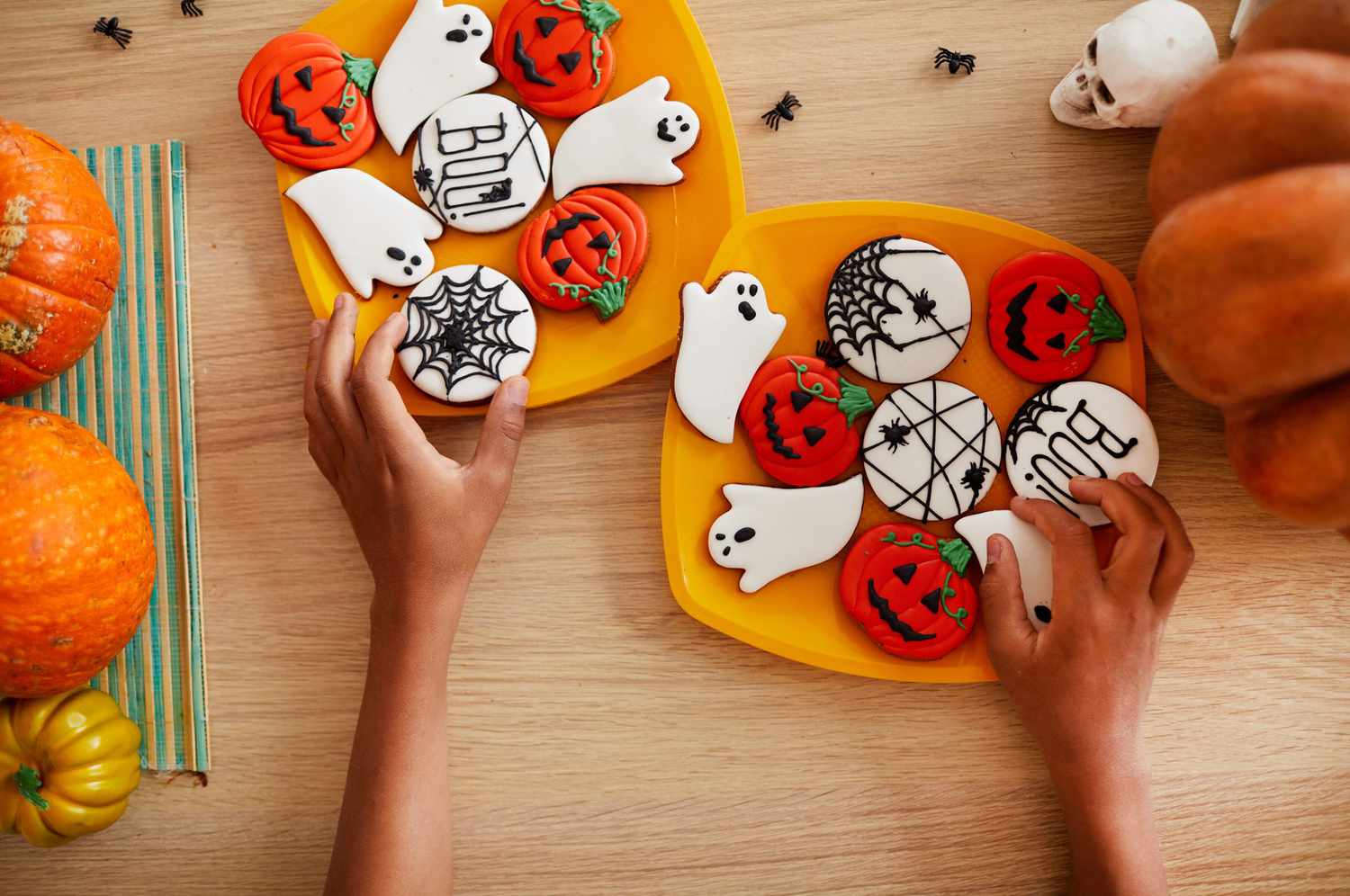 Directly above view of unrecognizable boy adjusting gingerbread cookies on plates while preparing sweets for Halloween party