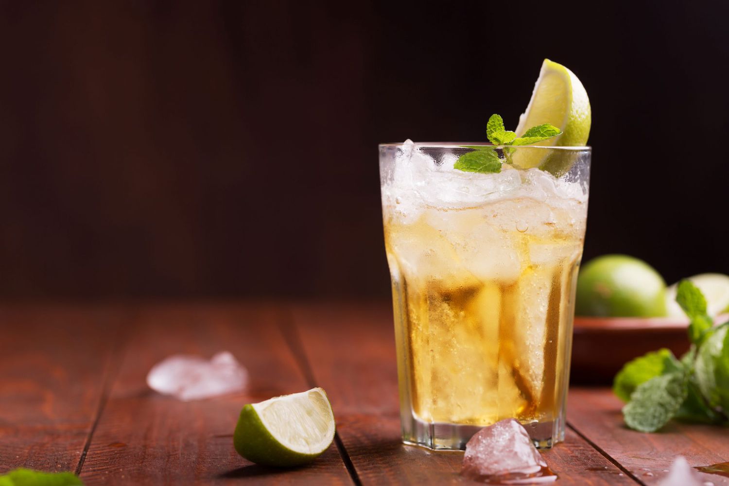 Glass of ginger beer with lime wedge garnish on wooden table
