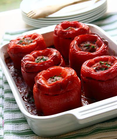 a white ceramic baking dish holding 6 baked stuffed red bell peppers