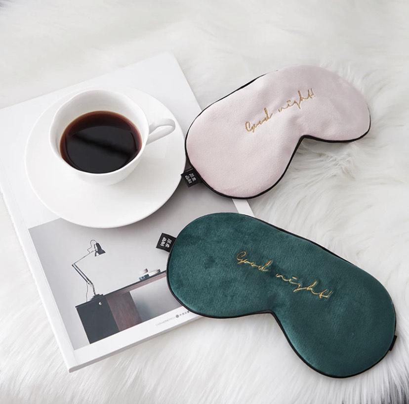 One green and one pink velour eye mask that says "good night" in gold typeface next to cup of coffee/tea
