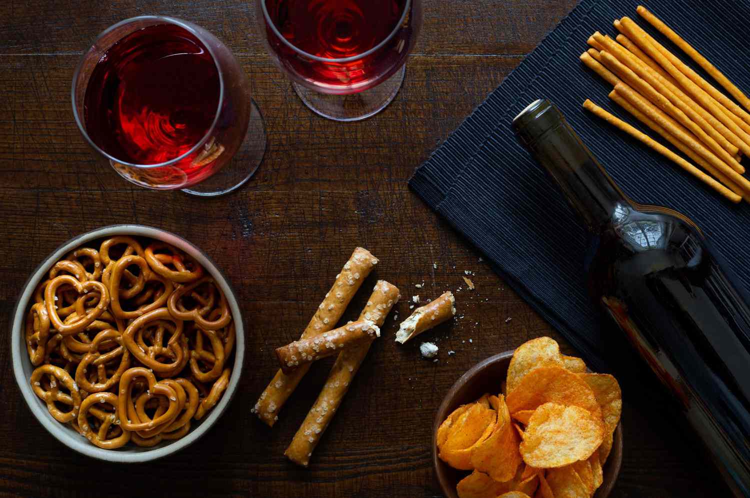 Red wine with savoury party snacks on rustic dark wood background from above.