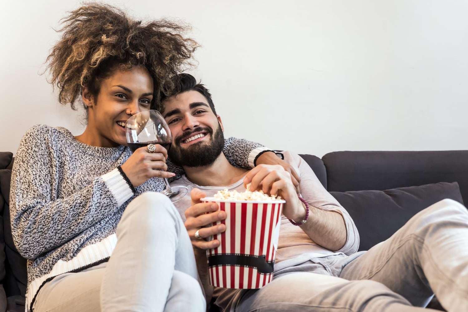 Happy mixed race couple watching TV and eating popcorn
