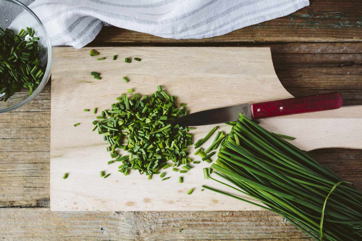chopped and whole fresh chives on cutting board with knife