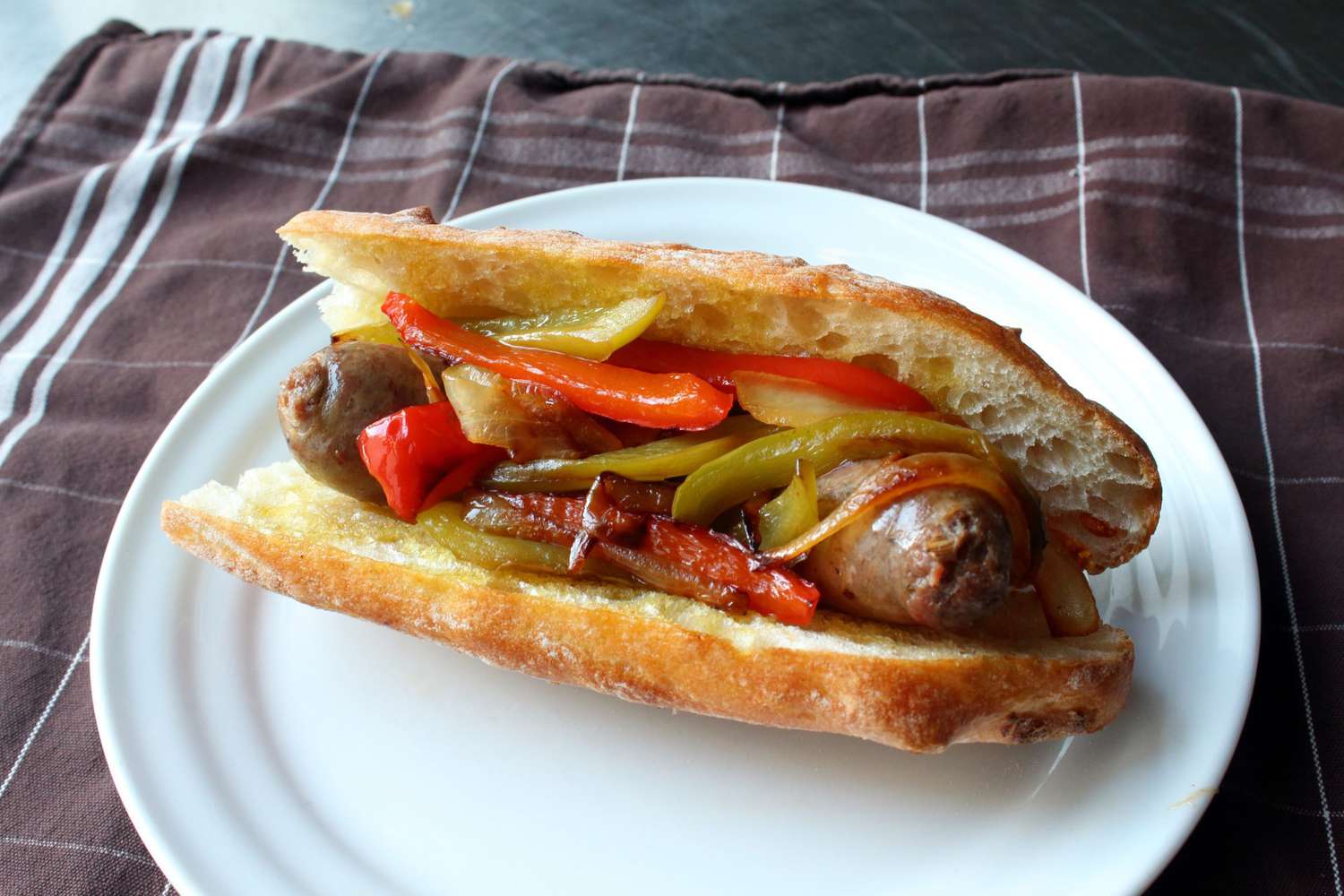 top-down view of a sausage link with onions and peppers in a bun