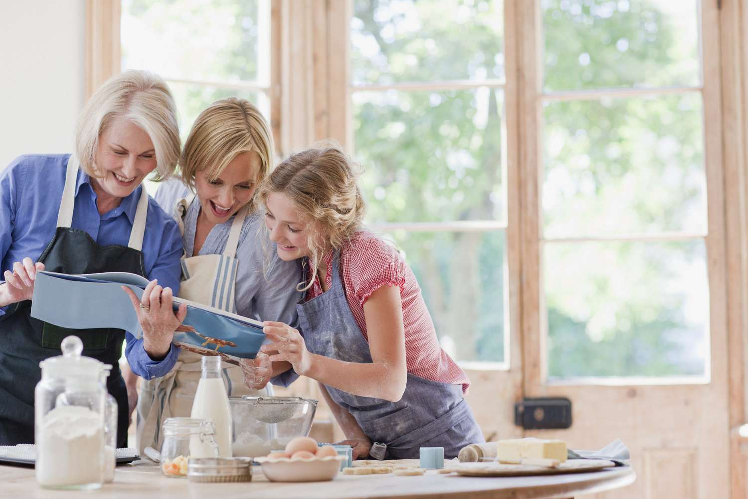 Multi-generation females looking at cookbook and baking in kitchen