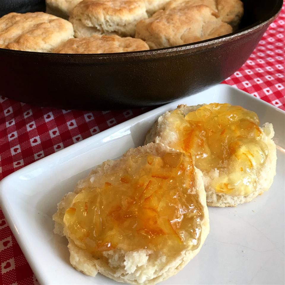 biscuits smeared with orange marmalade with additional biscuits in cast iron skillet in background