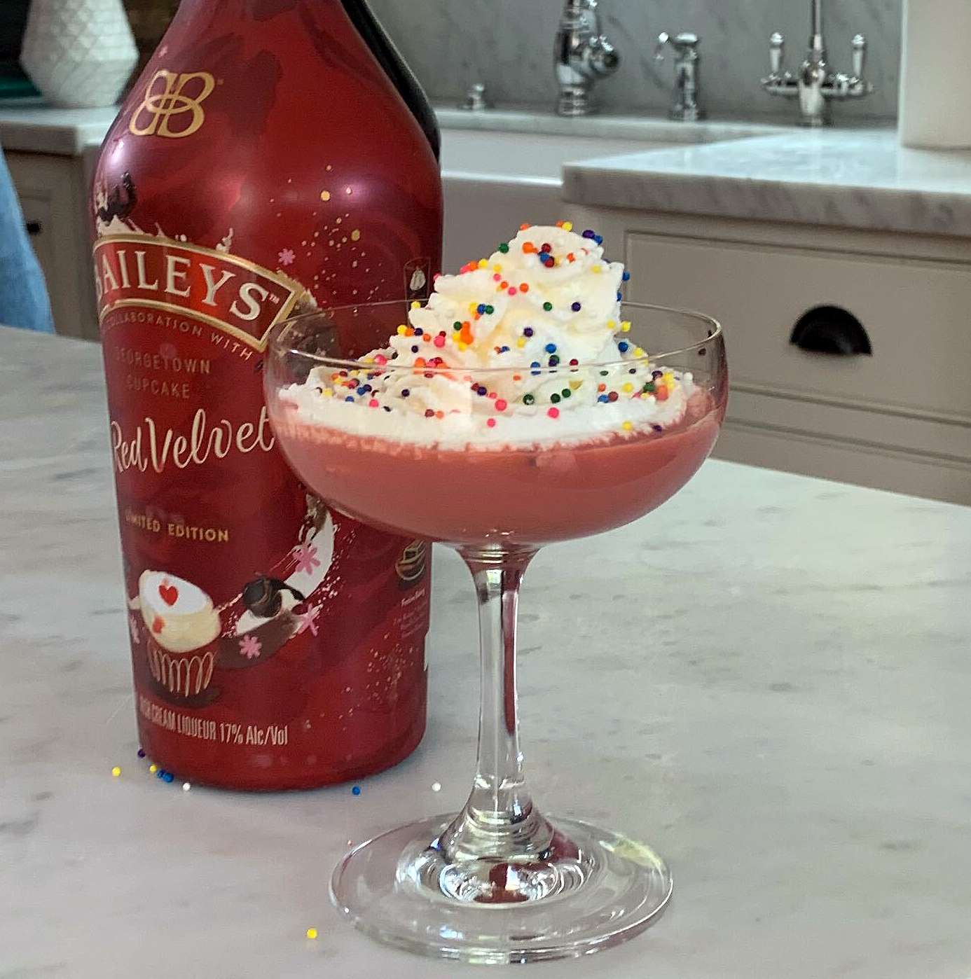 a pink cocktail topped with whipped cream and colored sprinkles