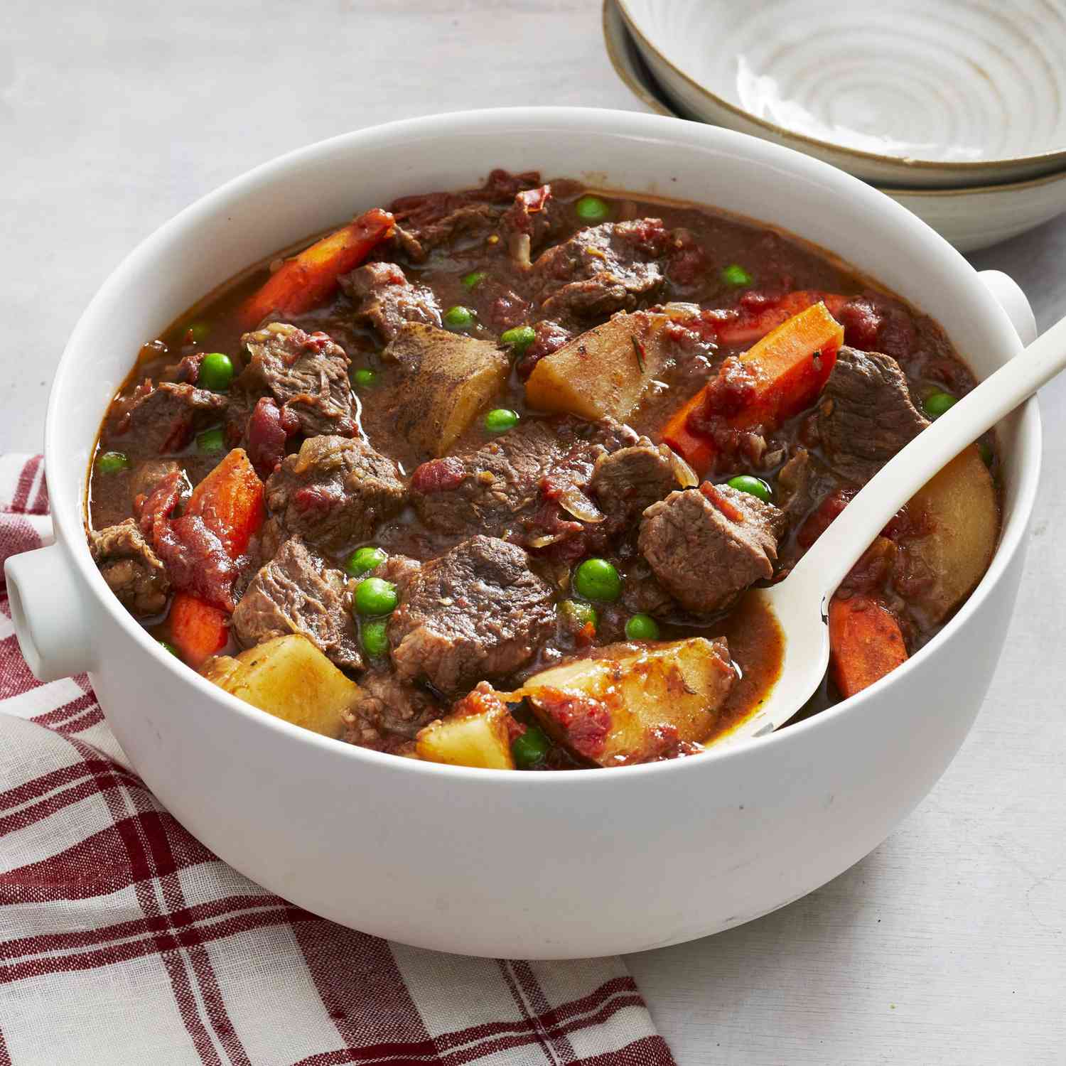 Deep white bowl of beef stew with a white spoon nestled in.