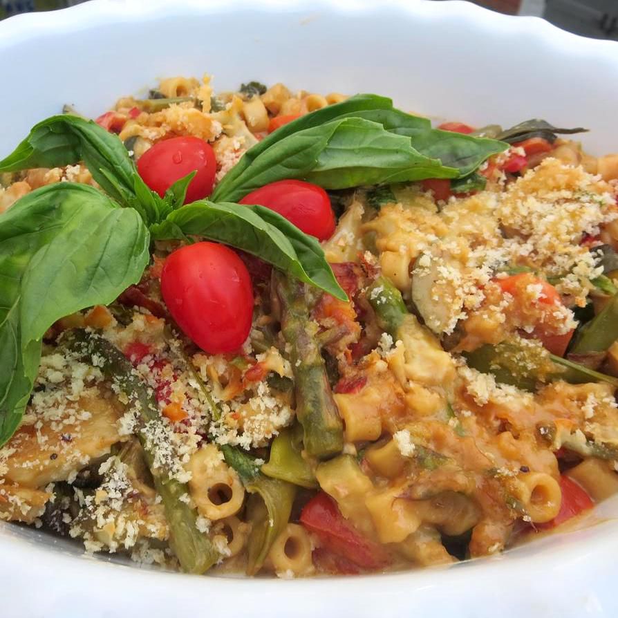 primavera pasta casserole in a white dish topped with basil and tomatoes