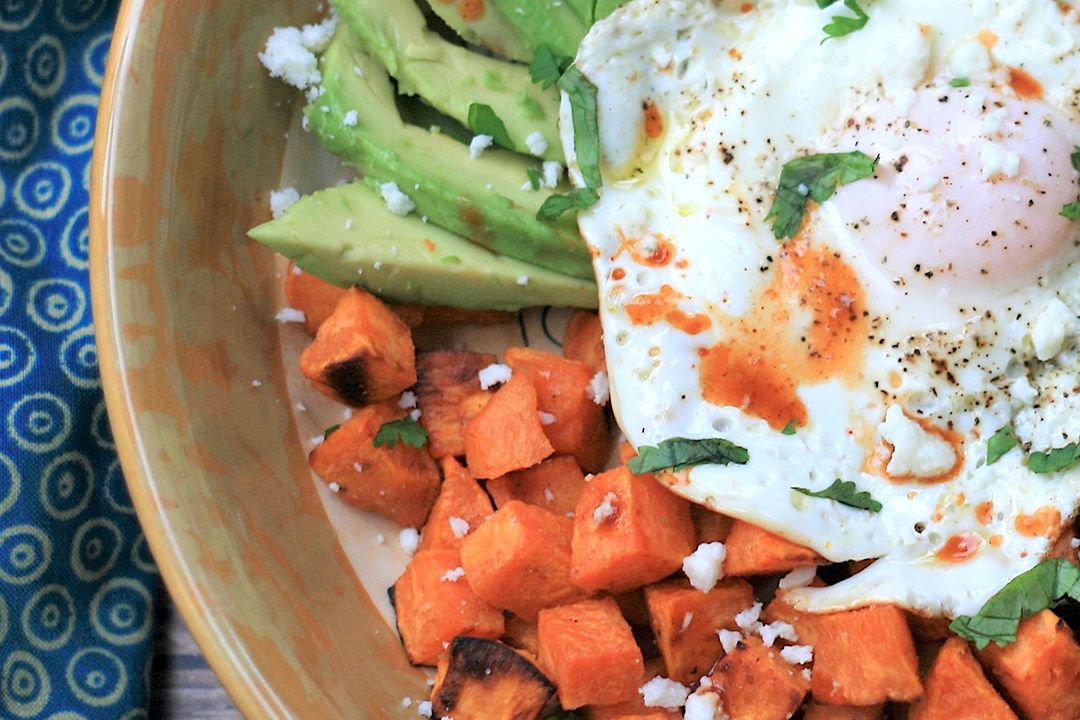 breakfast bowl with cubed sweet potatoes, avocado slices, ground meat, black beans, and an egg