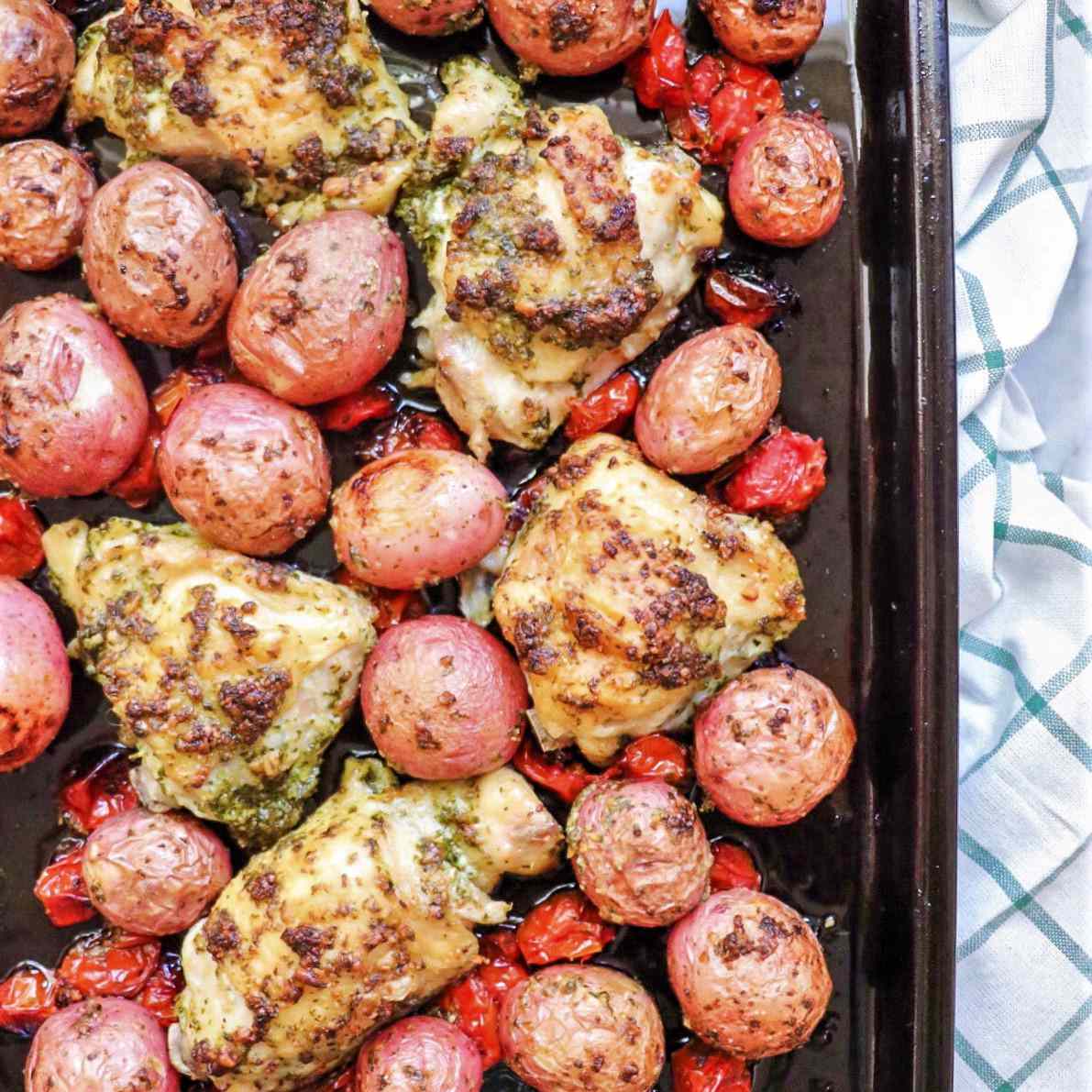 Sheet pan with baked chicken thighs and potatoes tossed in pesto