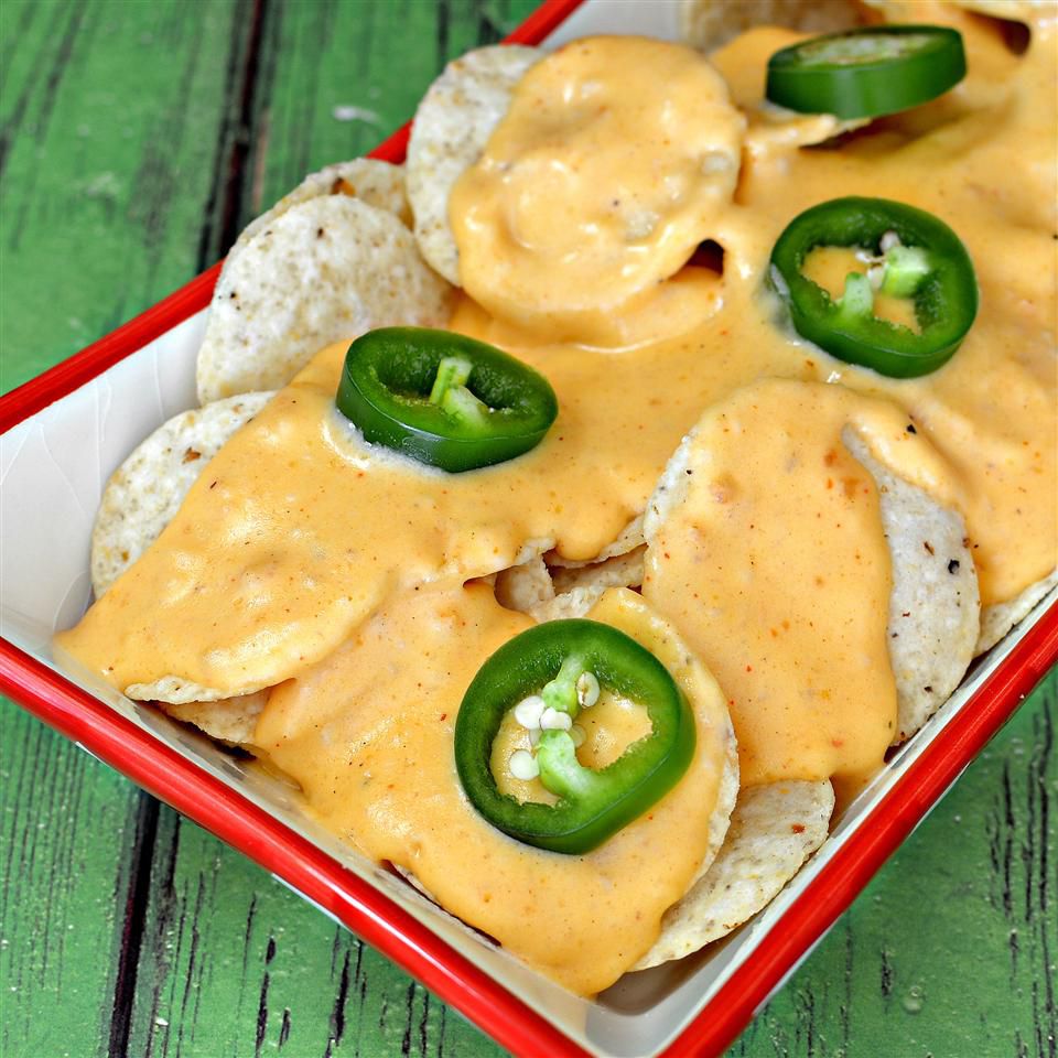 plate of tortilla chips topped with homemade nacho cheese sauce and sliced jalapeno peppers