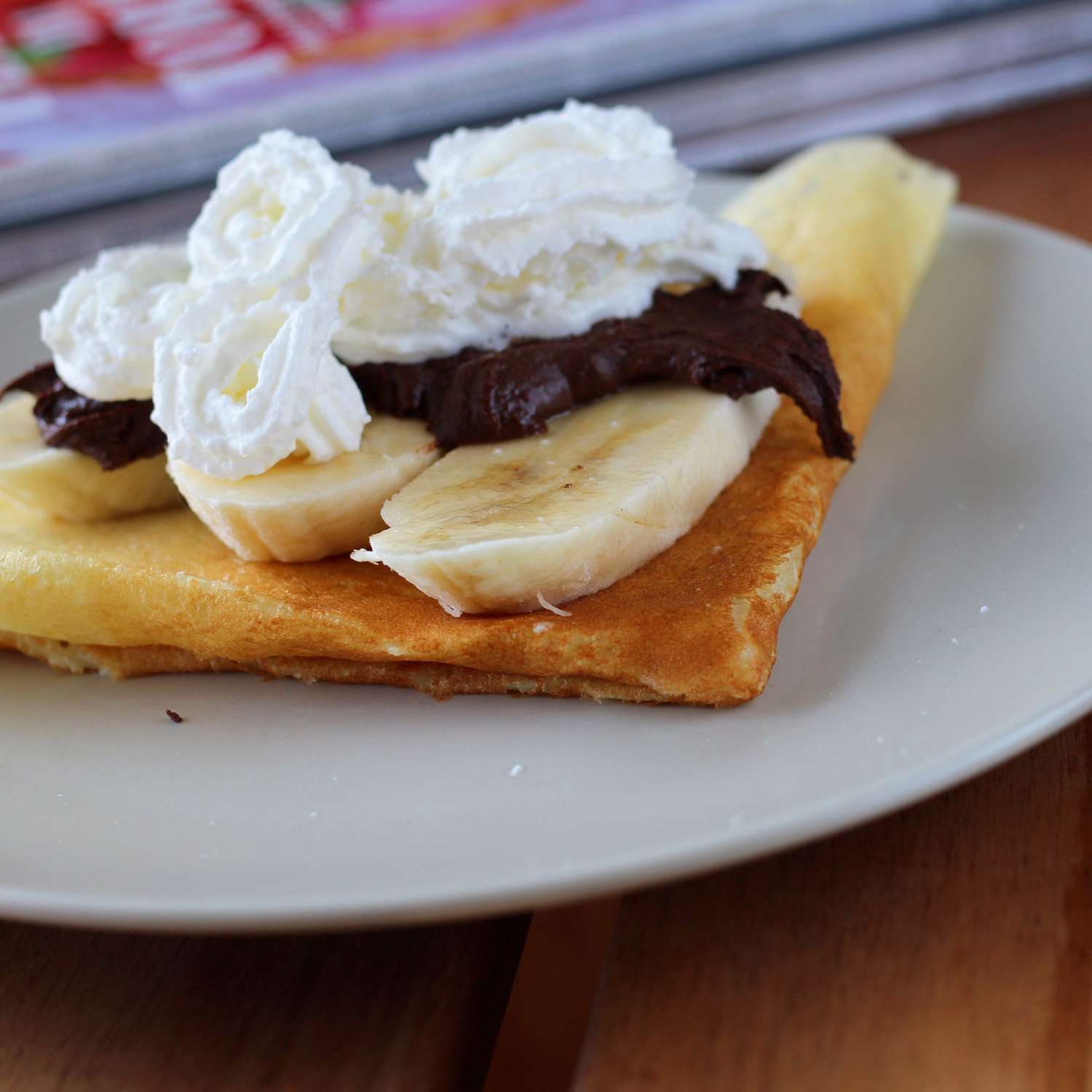 crepes with banana, chocolate sauce, and whipped cream on white plate