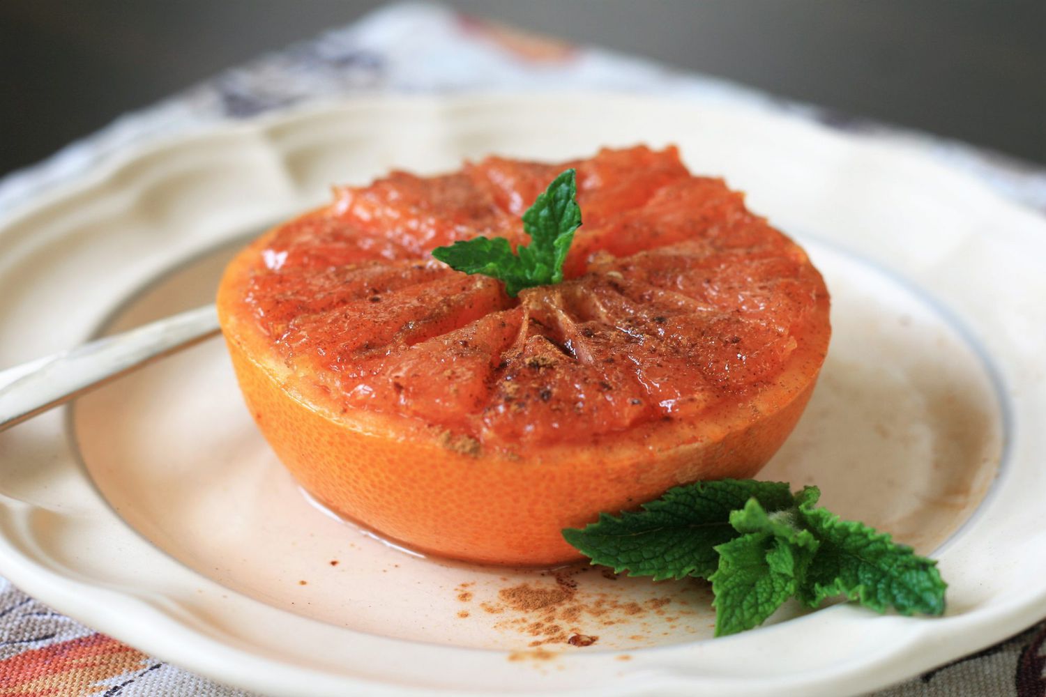 a grapefruit half sprinkled with brown sugar and cinnamon, garnished with a mint sprig, on a white plate