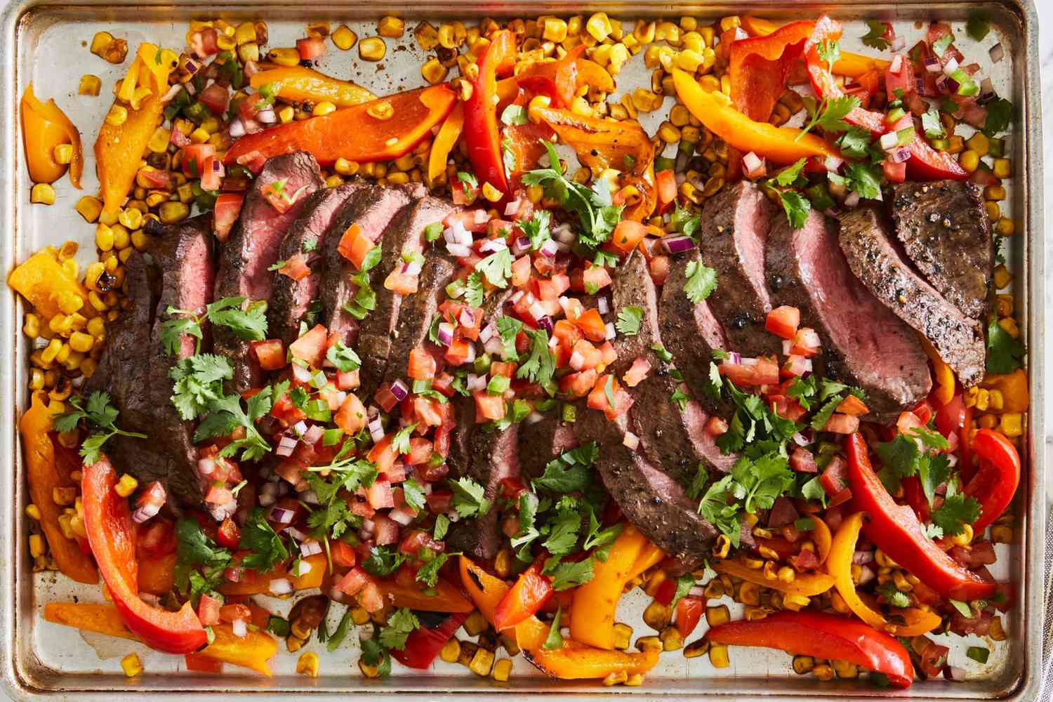 southwestern beef sheet pan dinner with sliced steak, corn kernels, bell pepper slices, pico de gallo, and cilantro leaves