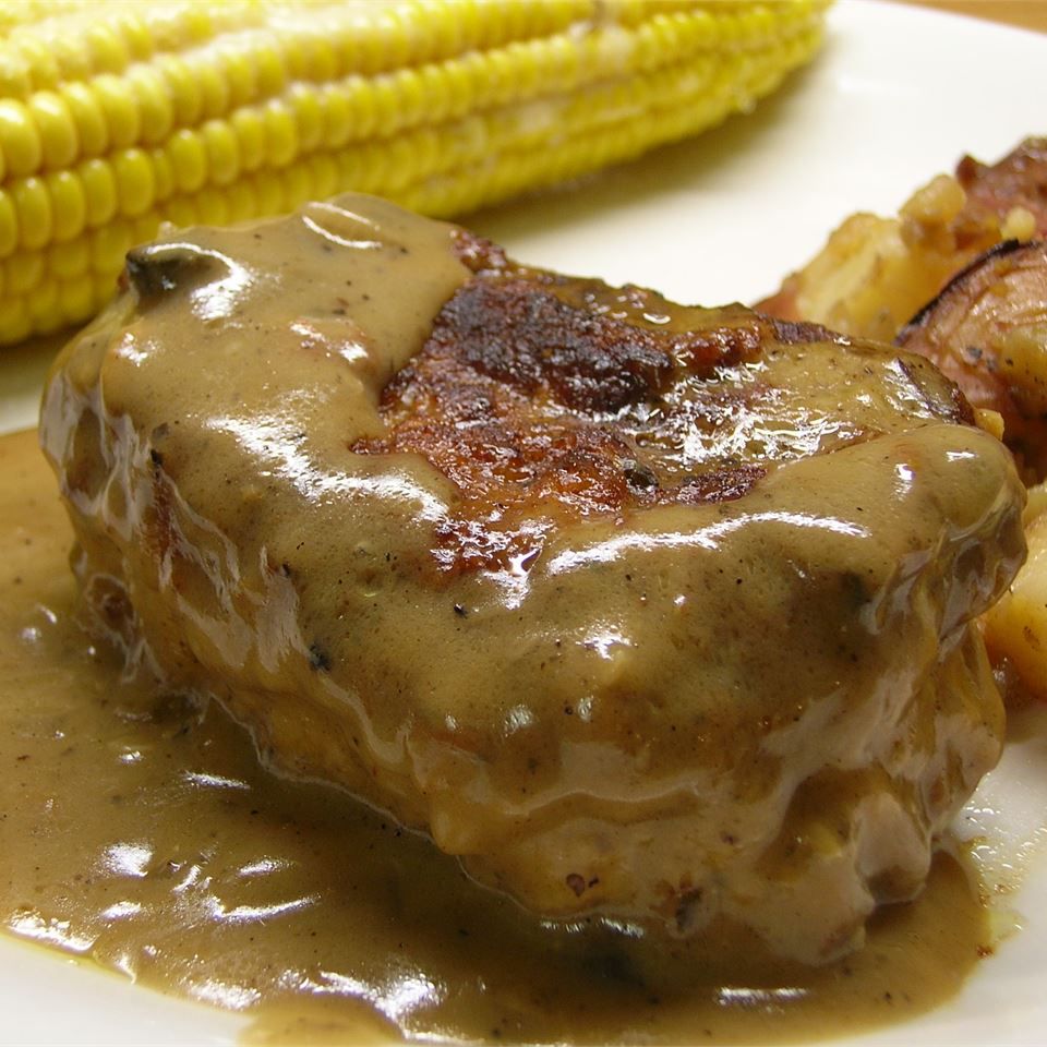close up of baked pork chop with mushroom sauce on a plate with potatoes and corn on the cob