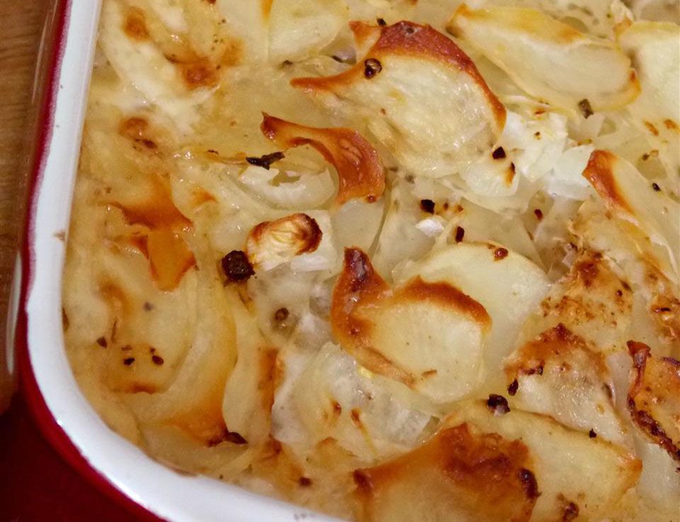 top-down view of a corner section of a baking dish with scalloped potatoes, baked until the edges are brown