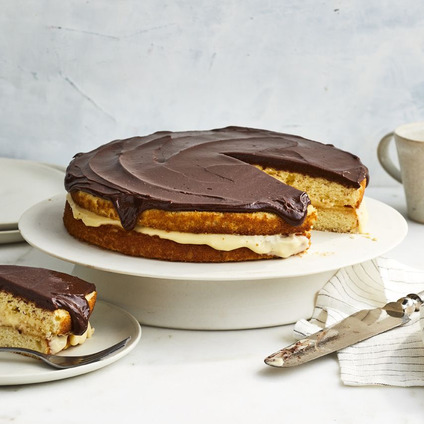 Beautiful layered Boston Cream Pie Cake on cake stand with a plated slice out nearby