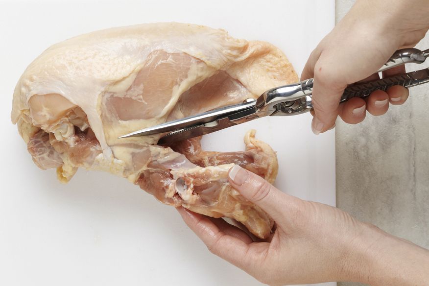 Using kitchen shears to remove the backbone from the chicken carcass after legs and wings have been removed